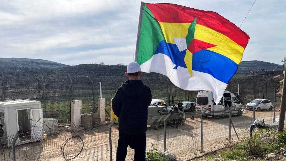Boy holds a large Druze flag as he looks out towards the ceasefire line between the Israel-occupied Golan Heights and Syria (file photo)