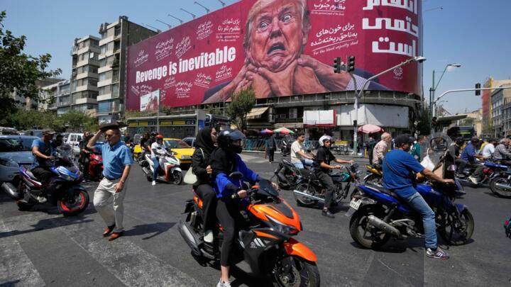 Motorcyclists pass a billboard depicting US President Donald Trump with hands around his neck beneath the words "Revenge is inevitable" in Tehran, Iran, August 24, 2026.