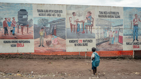 Un enfant rentrant de l'école s'arrêtant pour regarder les illustrations de sensibilisation à Ebola affichées sur les panneaux du Centre de traitement d'Ebola (ETC) de Munigi, le 2 juin 2026.