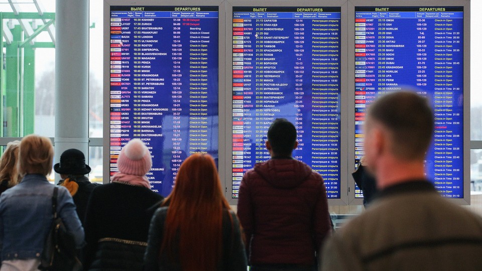 A crowd of passengers staring at flight departure screens in an airport