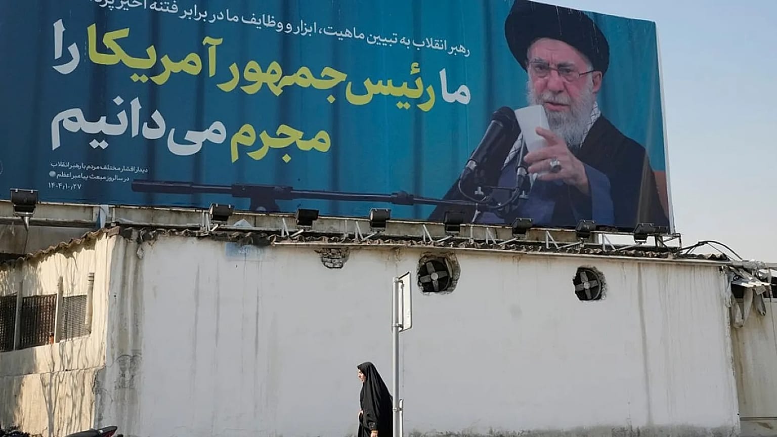  امرأة تمر أمام لوحة إعلانية تحمل صورة المرشد الأعلى الإيراني آية الله علي خامنئي مع اقتباس له يقول: "نعترف بأن رئيس أمريكا مجرم"، في طهران، إيران، الثلاثاء 17 فبراير 2026. 