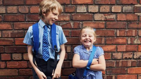 Two happy smiling school children on their way to school wearing blue school uniforms 