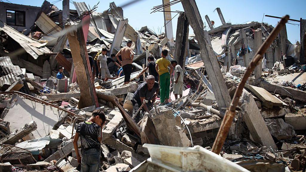 Palestinians stand on rubble and metal at the scene of an Israeli air strike in Bureij refugee camp, central Gaza (25 August 2026)