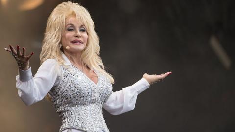 Dolly Parton wears a white shirt and bedazzled white and silver waistcoat.