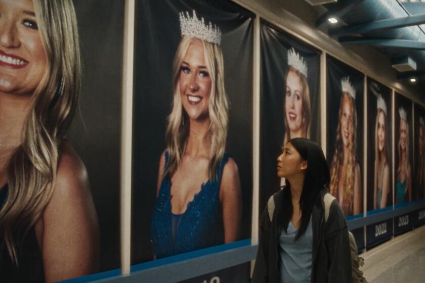 An Asian high schooler looks up at posters of white prom queens.