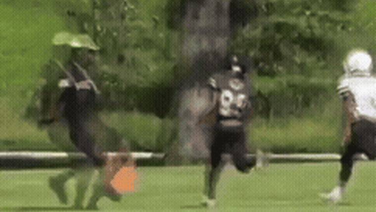 A GIF from a video showing a coach tripping a child football player outside on a field