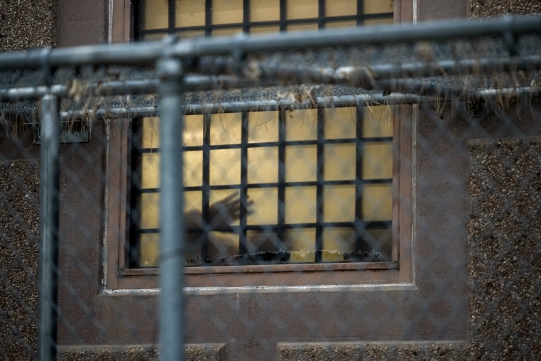 The silhouette of a person waving behind a barred window.