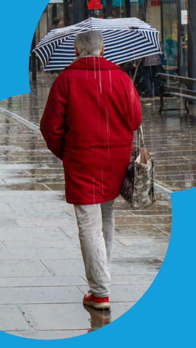 A woman in a red coat walks in the rain