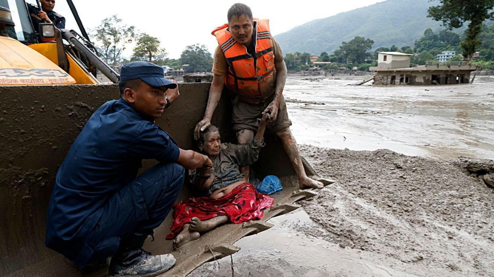 Rescuers transport an elderly woman on heavy machinery amidst flash floods