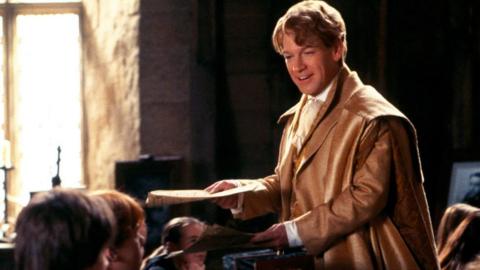 Kenneth Branagh as Gilderoy Lockhart wears a brown jacket and smiles. SINGLE USE