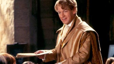Kenneth Branagh as Gilderoy Lockhart wears a brown jacket and smiles. SINGLE USE