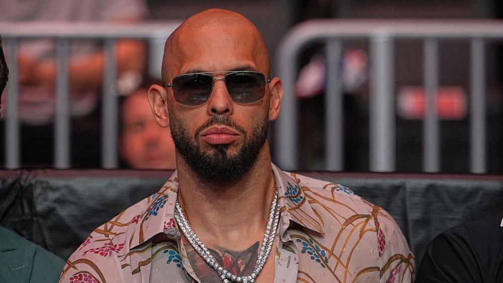 Andrew Tate wearing a colorful shirt and glasses at a UFC event in April