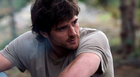 Jacob Elordi appears dishevelled with shaggy hair, a beard and wearing a light green t-shirt.