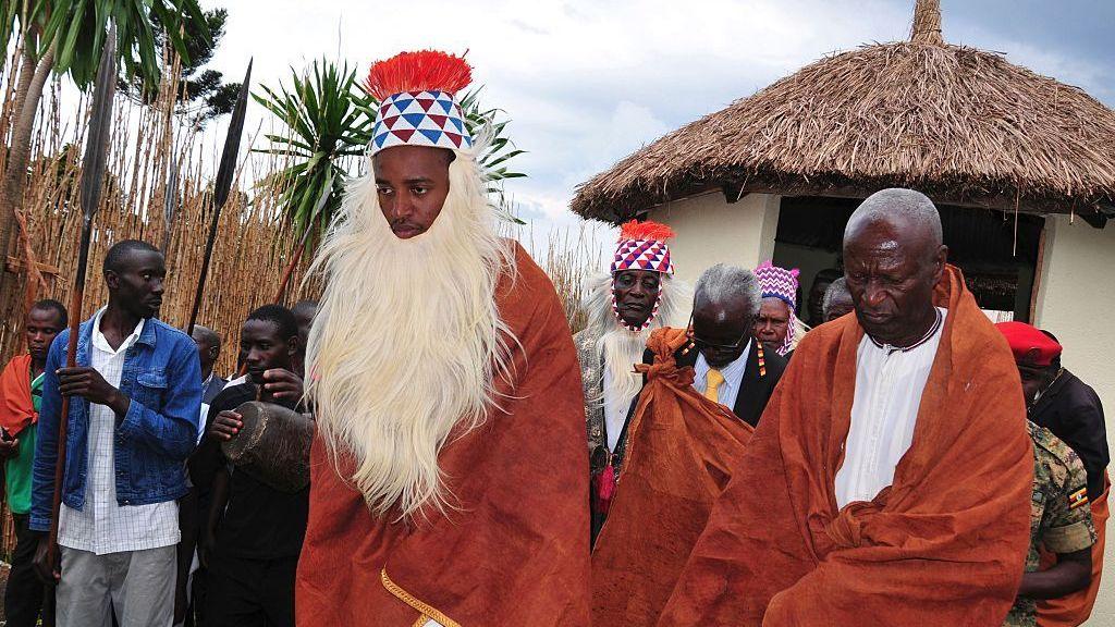 King Oyo takes part in a traditional procession wearing a red cloak and long white fur around his chin.

