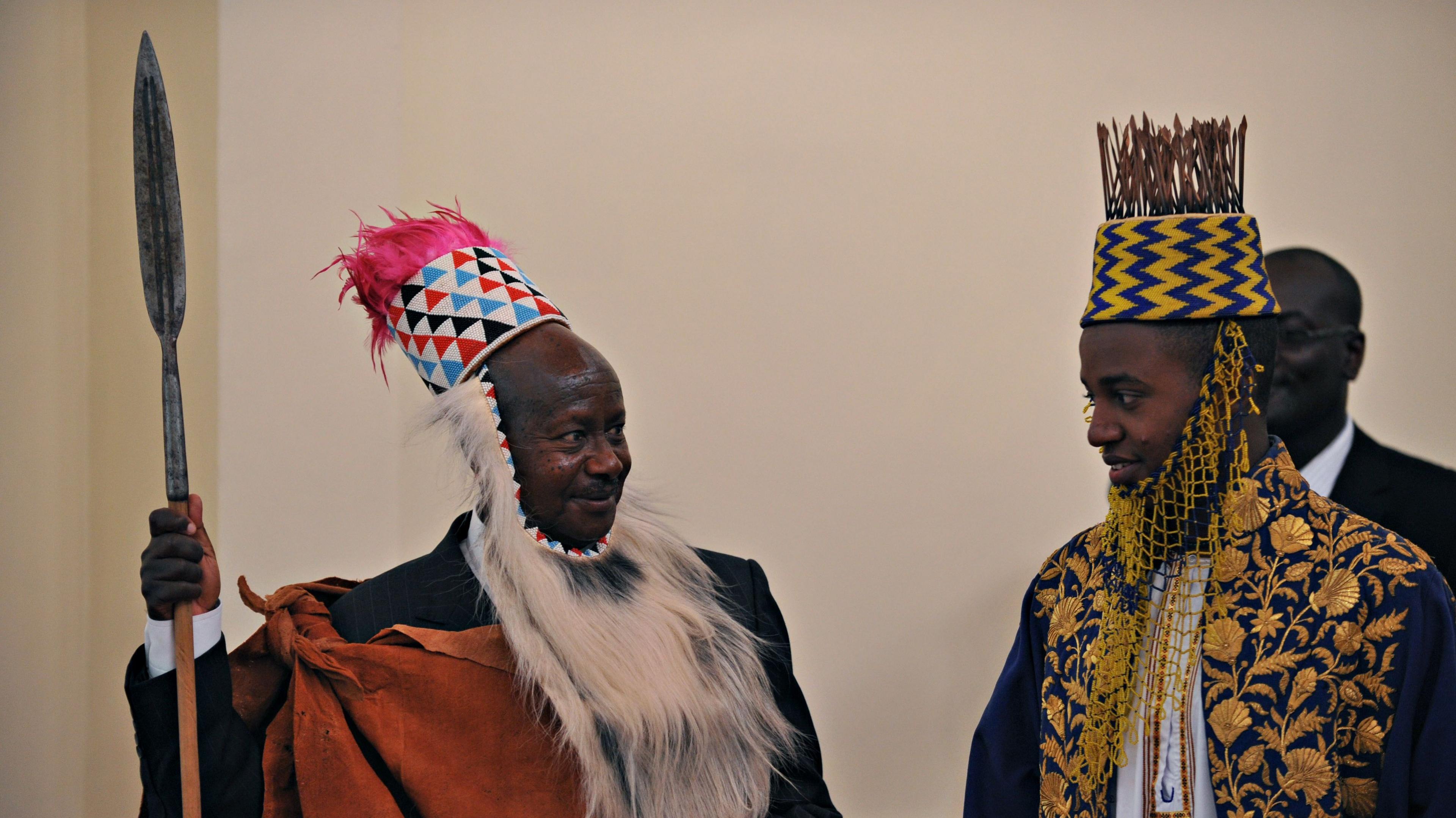Ugandan President Yoweri Museveni (L) wearing traditional Toroo kingdom ceremonial head gear smiles at Ugandan King Oyo
