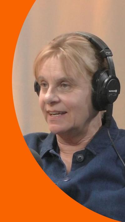A woman with blonde hair wearing a blue shirt sits in front of a microphone
