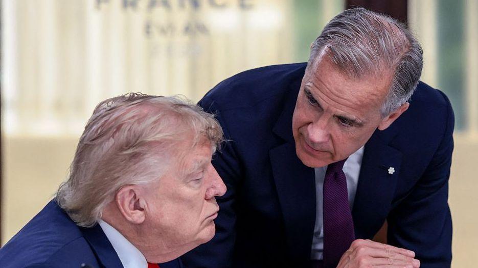 US President Donald Trump (left) speaks with Canada's Prime Minister Mark Carney during a work lunch as part of the G7 summit, in Evian, eastern France, on June 16, 2026. Trump is sitting down while Carney is standing over but leaning into the conversation. 