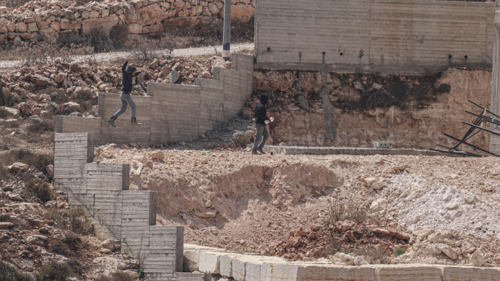 Israeli settlers jump over the garden wall as they make their way towards a Palestinian home under construction in the village of Qusra, which has faced escalating settler violence over the past month.