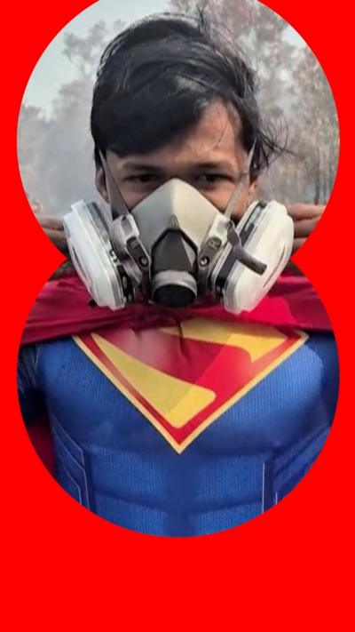 Teenage boy wearing a superman costume and gas mask standing in land burnt by wildfires