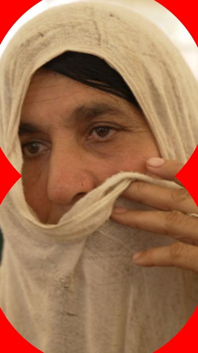 A woman holds a white shawl over her head and face