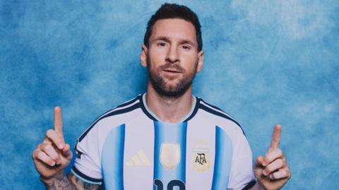 Lionel Messi poses in a photoshoot, with the index fingers of both hands pointing upwards