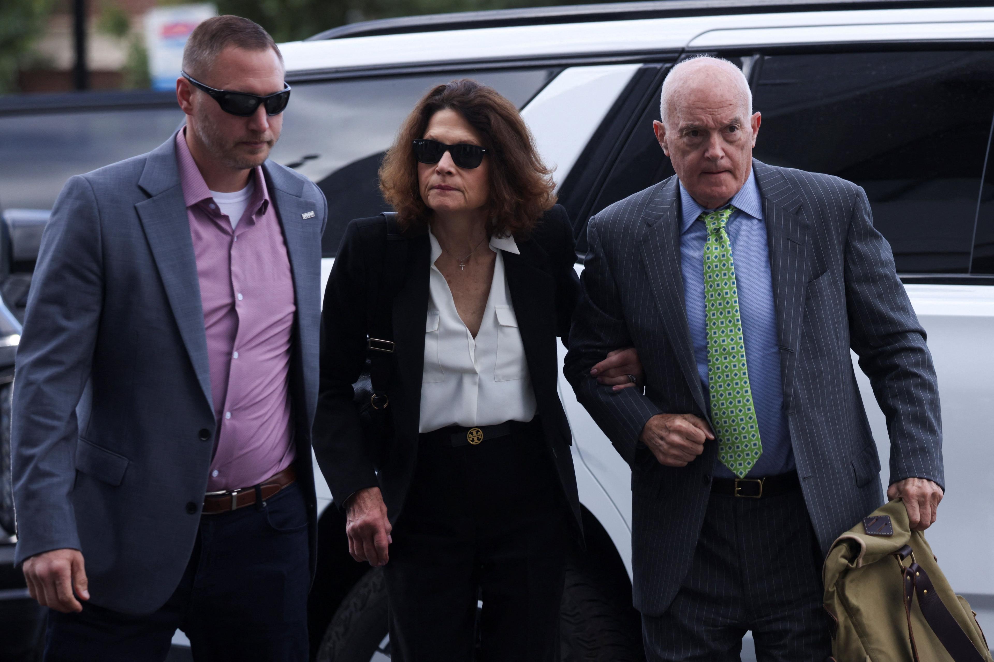 Charlie Kirk's mother, Kathryn, wears sunglasses and a dark suit over a white blouse as she holds the arm of her husband, Robert, wearing a pinstripe suit and green tie while they arrive at the Utah courthouse on Tuesday