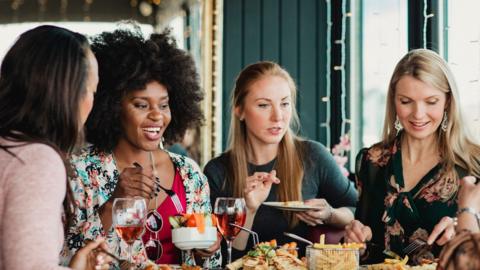 Group of four young women eat at a restaurant 