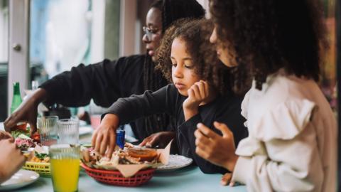 Stock photo shows a young family eating out at a restaurant, including children and adults.
