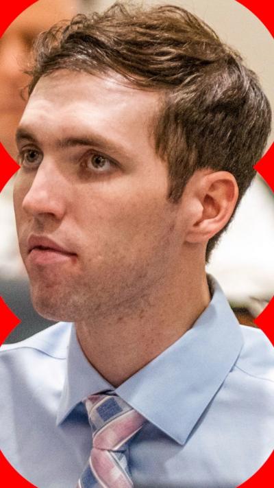 A man with short brown hair, wearing in a blue shirt with a tie.