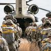 Paratroopers jump from a helicopter. 