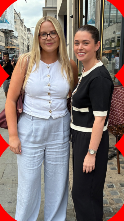 Two women stand in the street. One wears a white top, the other wears black and white.
