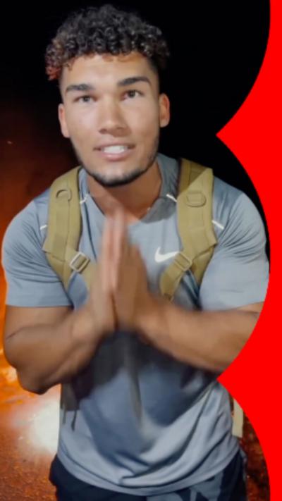 Man with short curly hair leans towards the camera with his hands together at his chest.