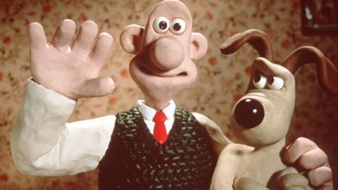 A stopmotion character of Wallace is waving and smiling at the camera with his arm round Gromit. Gromit the dog is giving him some serious side eye