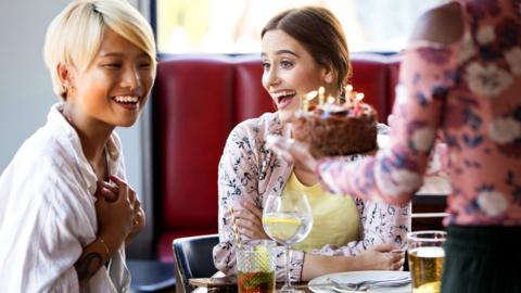 Excited young women friends celebrating birthday with cake in restaurant