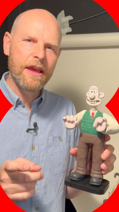 A man in a blue shirt holds up a Wallace figure from Wallace and Gromit.
