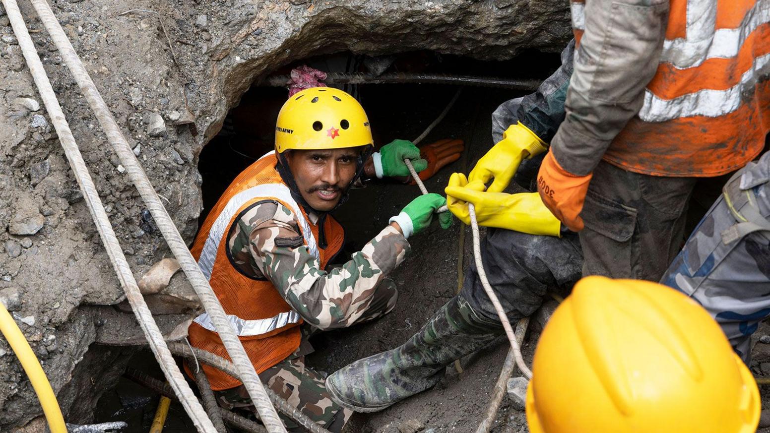 Rescue workers in yellow hard hats descend a tunnel with ropes in nepal 