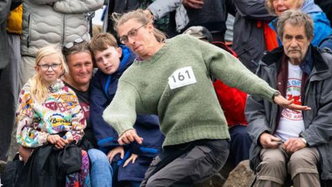 A man in a green pullover with 161 pinned to it is seen having just released a stone in the contest