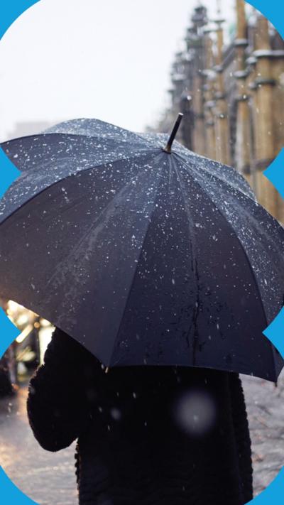 A person holding a black umbrella stands in the rain