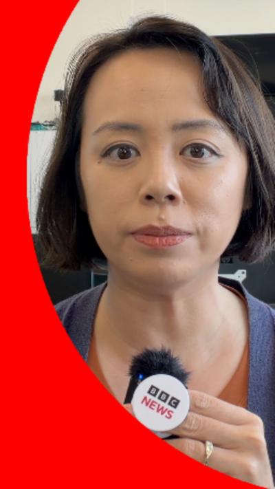 BBC Journalist, Tessa Wong, has short dark hair and is wearing a purple jacket over an orange top.