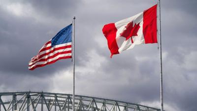 An American and Canadian flag flutter on poles over a bridge.