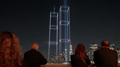 A group of people watching a drone light display showing the Twin Towers.