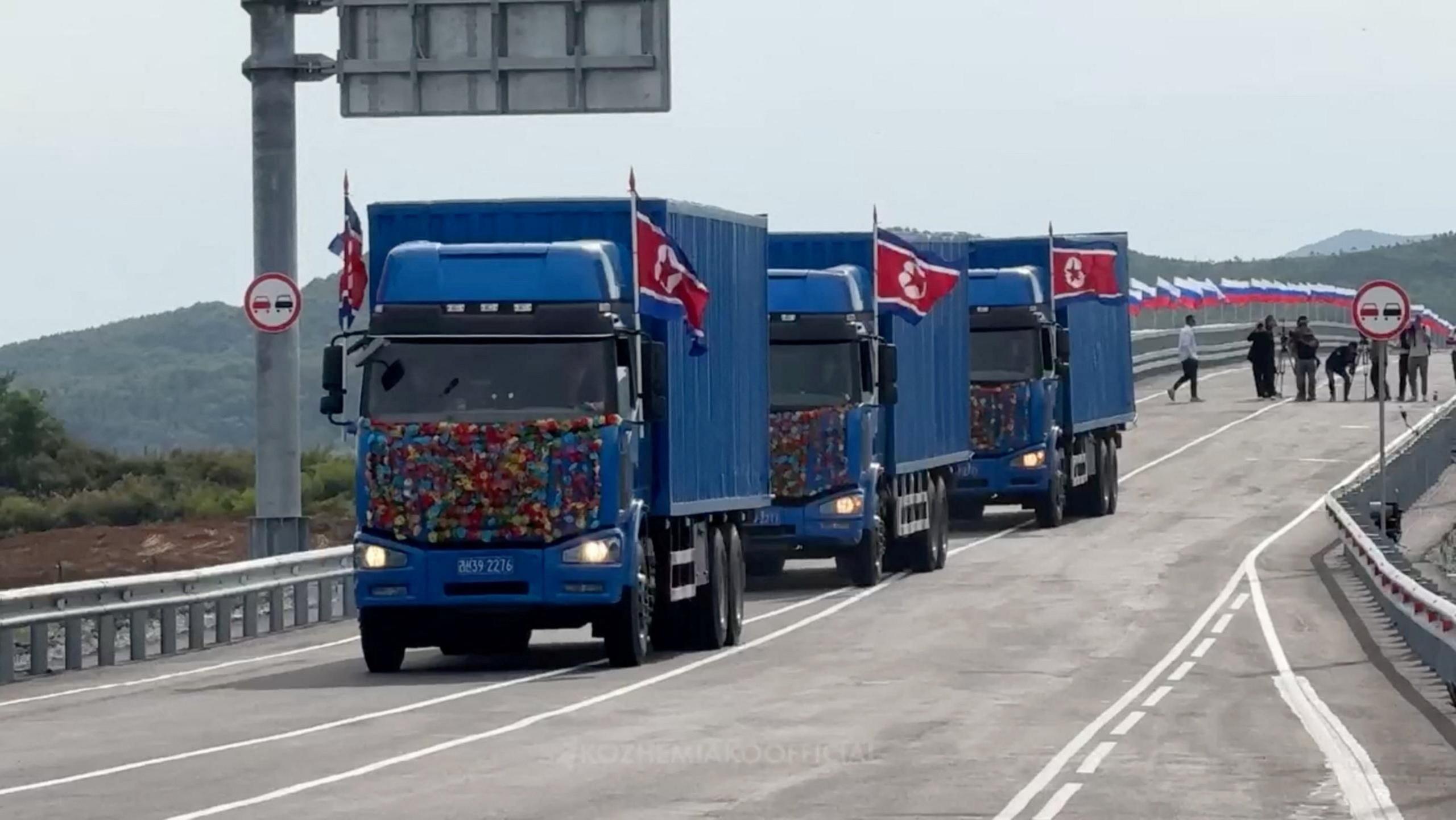 Blue trucks drive along a road during a ceremony opening the first road bridge between Russia and North Korea across the Tumen River.