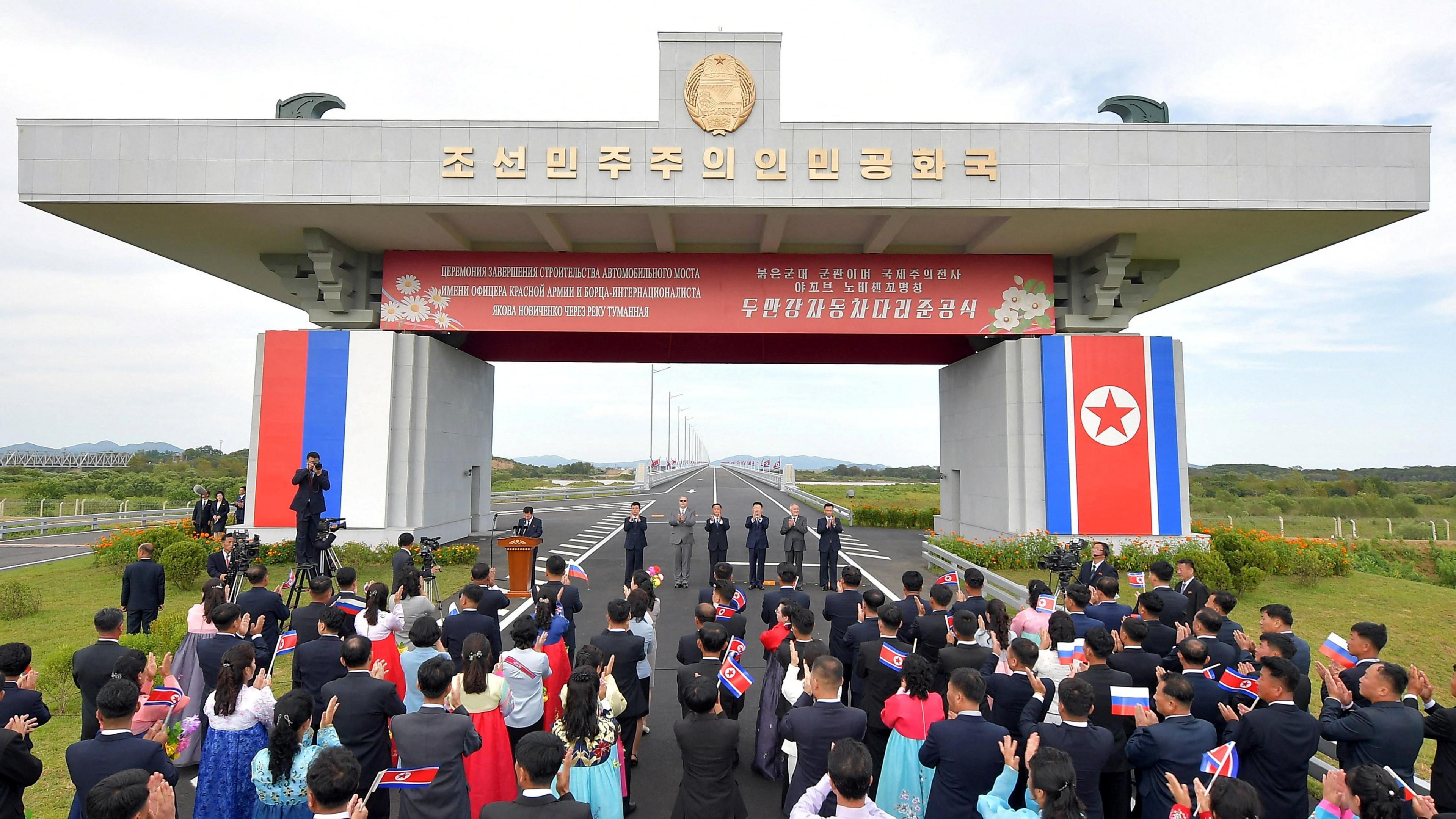 Attendees applaud as North Korea and Russia open their first road bridge, which continues into the distance. 