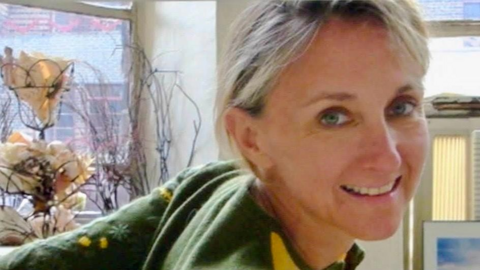 Karen Rowland smiling at the camera, wearing a green jumper with yellow flourishes. She has short mousey hair.