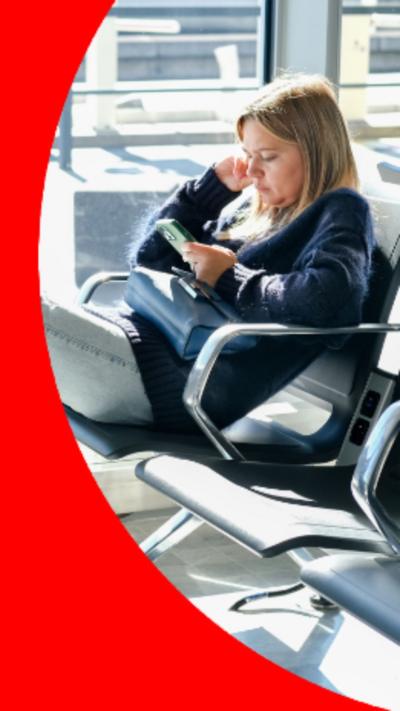A woman sitting on a chair in an airport waiting area, using her phone.