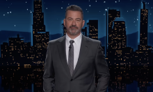 A man in a suit stands on a talk show stage.
