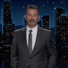 A man in a suit stands on a talk show stage.
