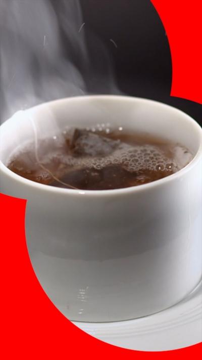 Close up of a steaming hot cup of tea in a glass cup with a tea bag steeping.