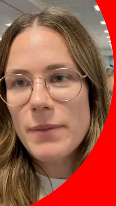 A woman with dark blonde hair and glasses talks to the camera