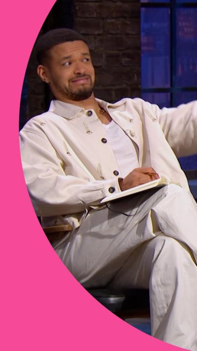 A man with short hair, a moustache and beard is sitting in a chair. He is wearing a white vest, jacket and trousers.